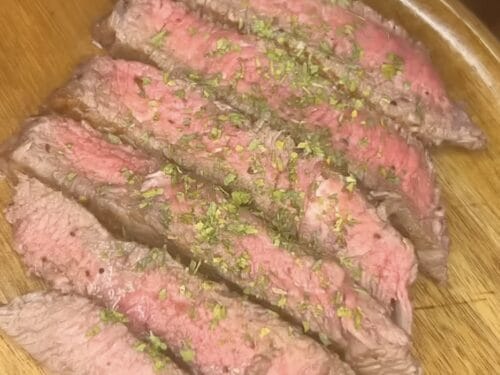 Four sliced pieces of pink-centered meat garnished with chopped green herbs on wooden surface